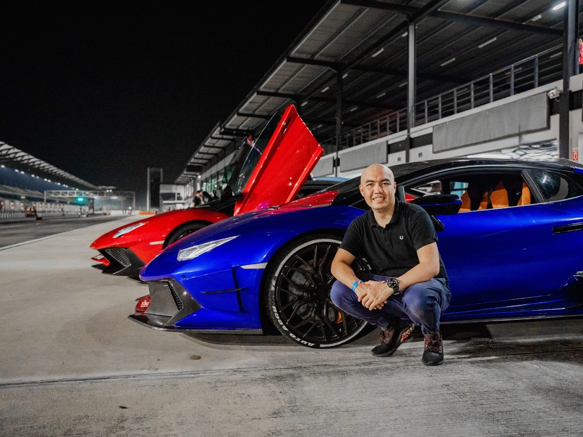 Nicky Lim crouched beside a blue Lamborghini Huracan on pit lane at night