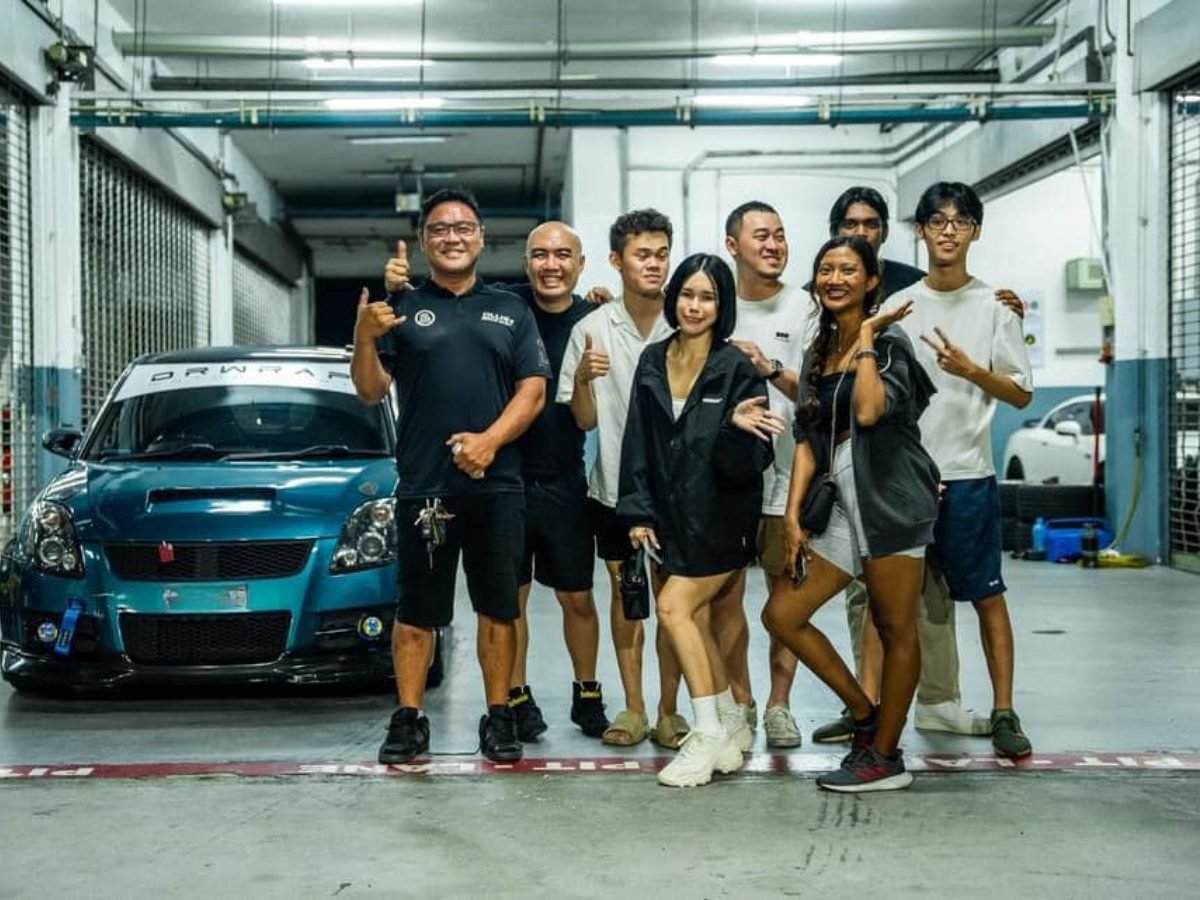 Group photo with a modified blue Suzuki Swift in a garage, everyone giving thumbs up