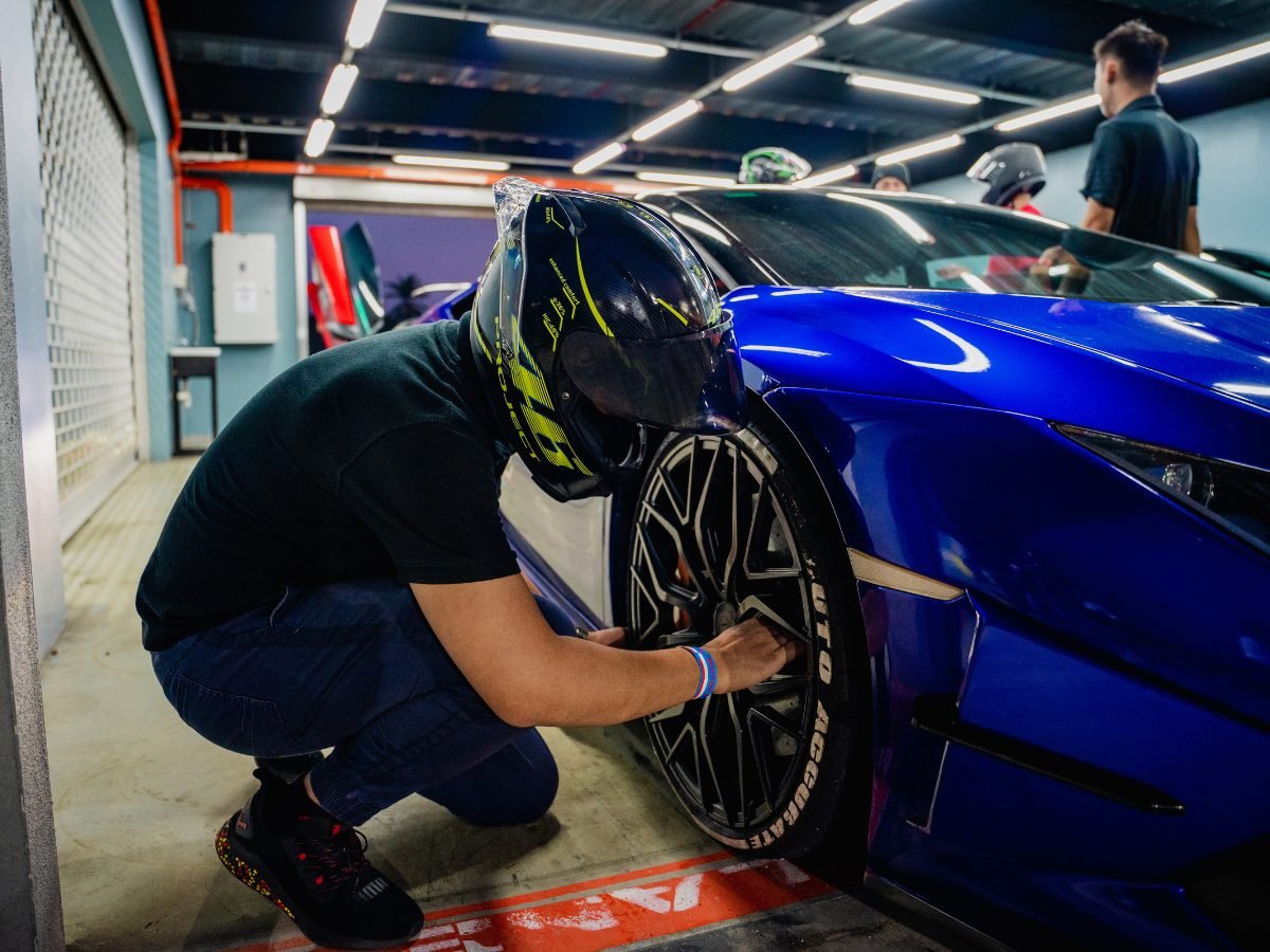 Nicky Lim in a helmet inspecting the wheel of a blue Lamborghini in the garage