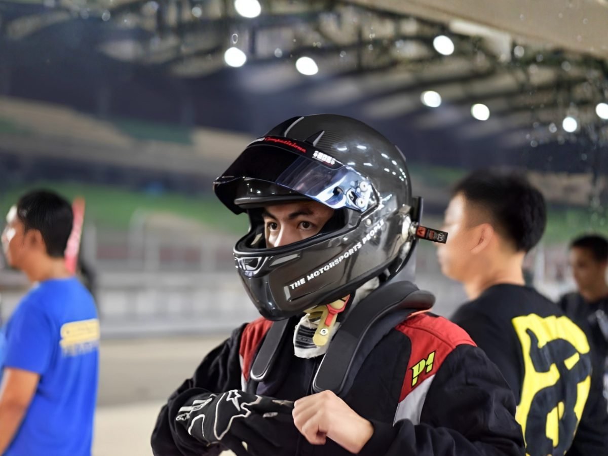Driver in full race helmet and harness looking over his shoulder in the paddock