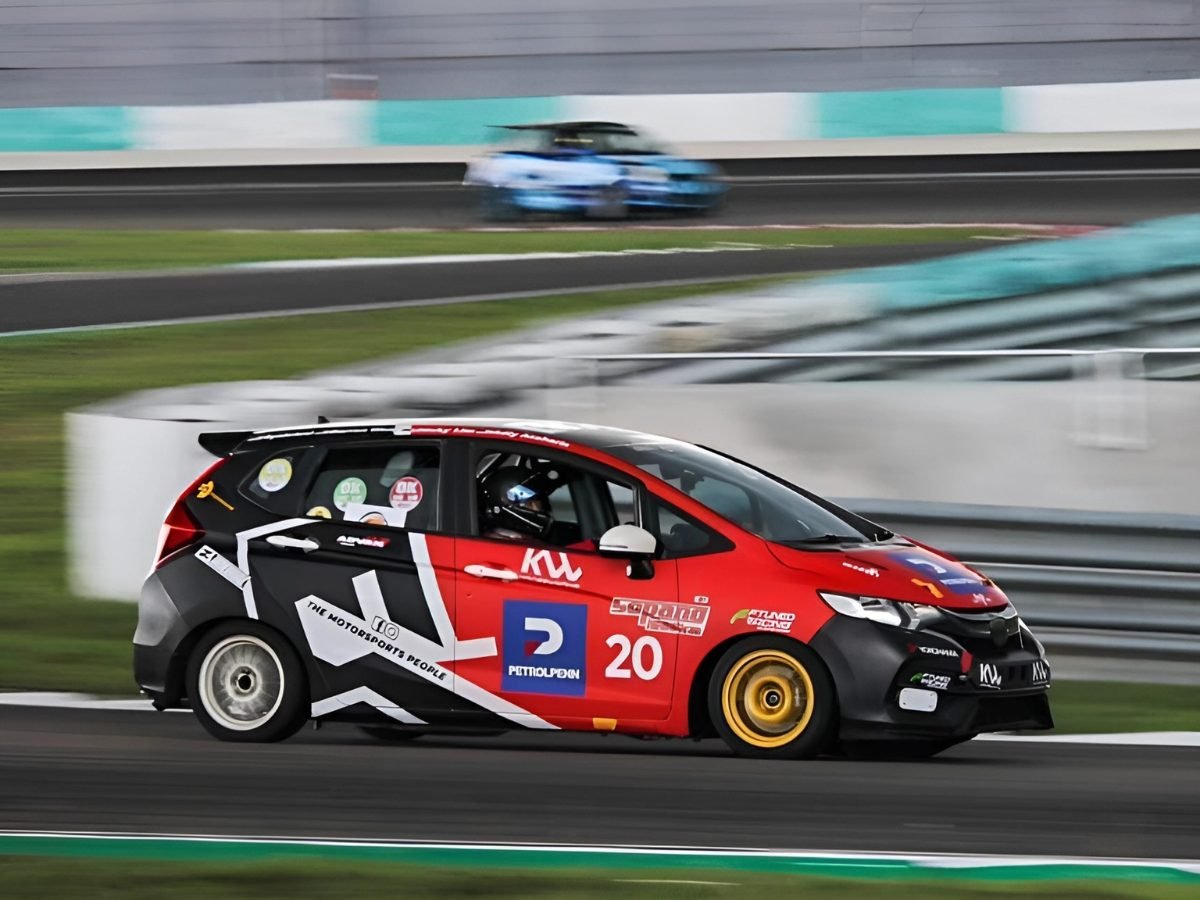 Red and black liveried race car number 20 on track with a blue car in the background