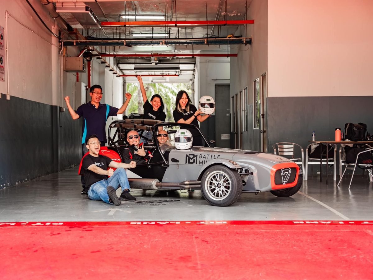 Group celebrating around a Caterham Seven in the garage, arms raised